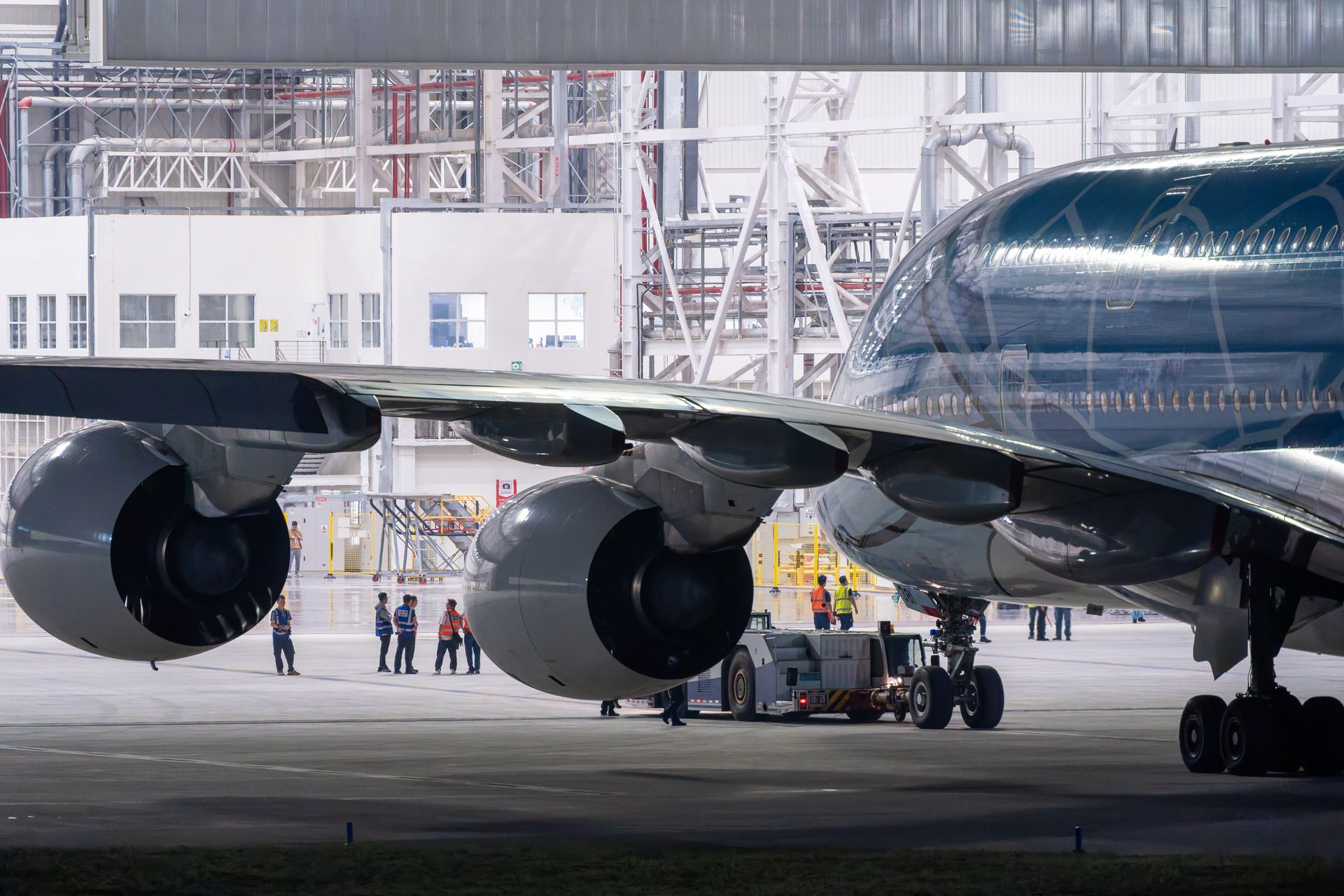 Crew members work beneath the engines of a commercial airliner inside a maintenance hangar