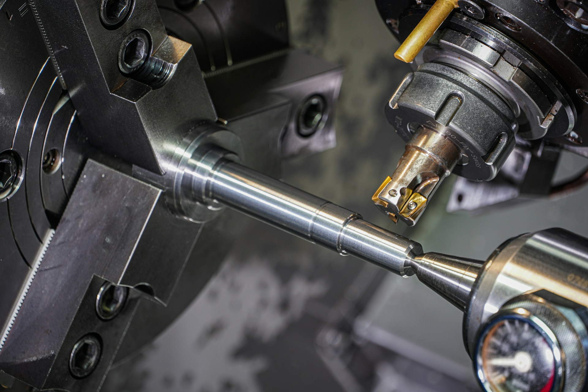 A precision turned shaft held in a CNC lathe chuck with a gauge in the foreground