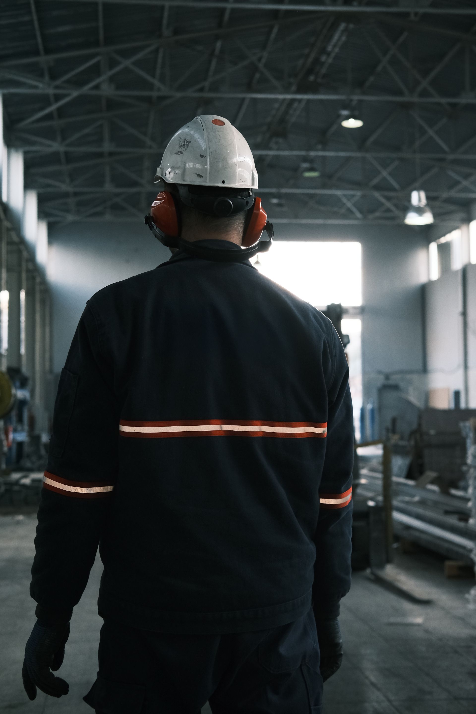 A worker in a hard hat, safety glasses and hi vis vest stands on a manufacturing floor