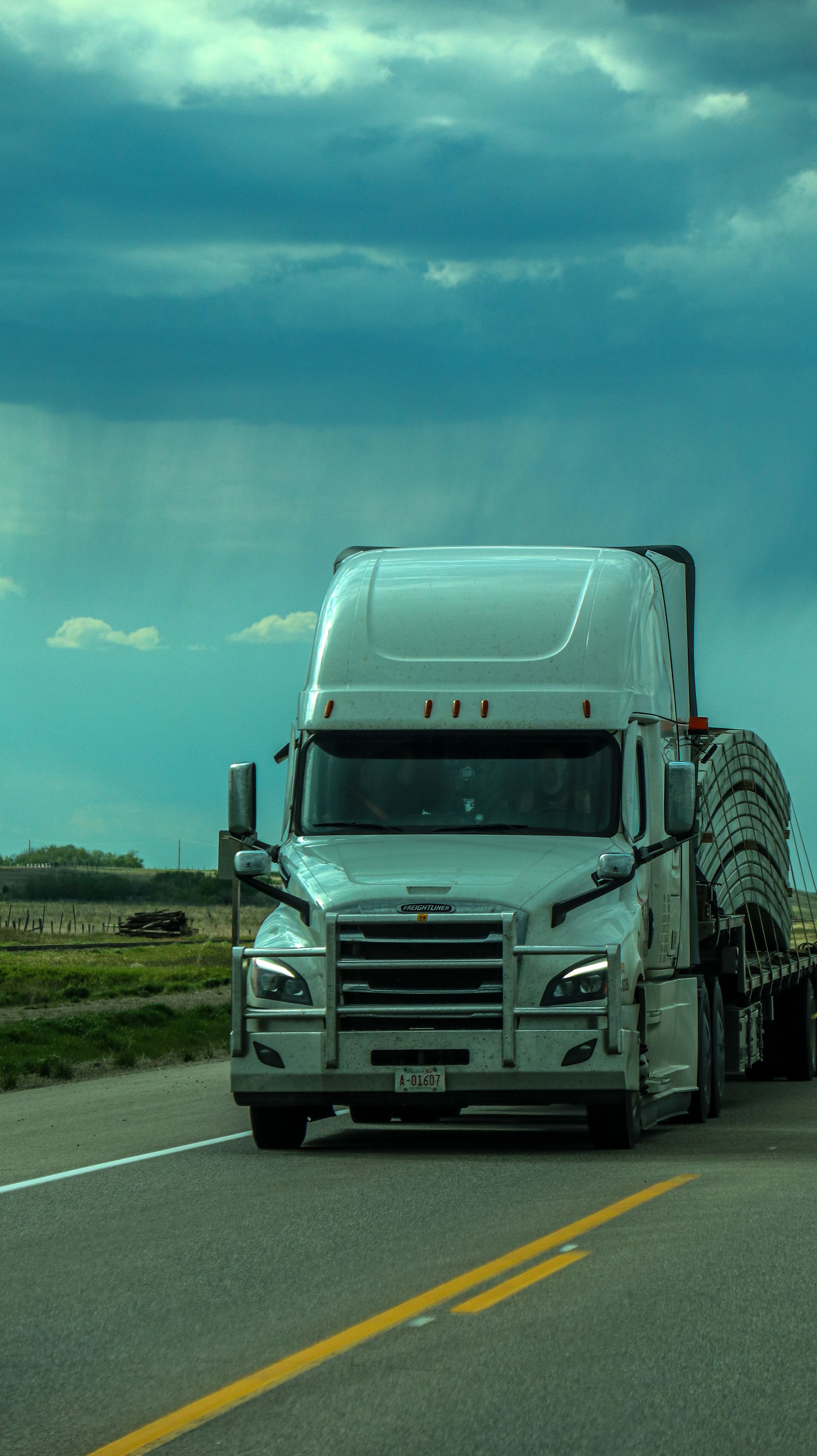 A semi truck travels an open highway under a dramatic sky
