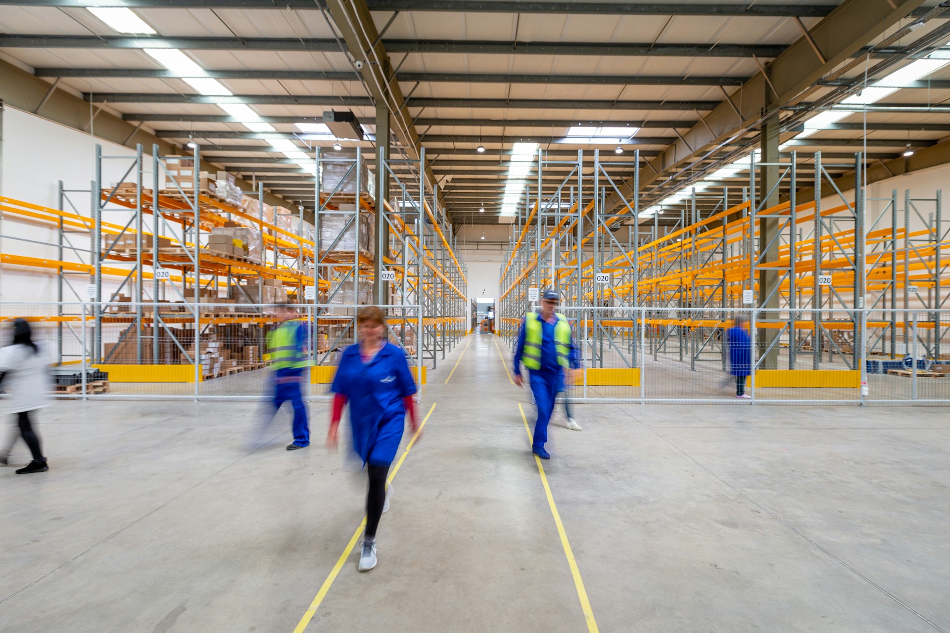 Associates in hi vis vests walk a distribution center aisle between racking