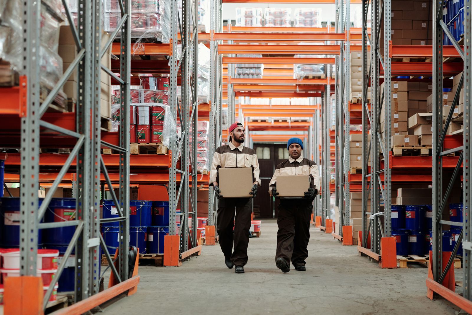 Two workers carry boxes between warehouse shelving