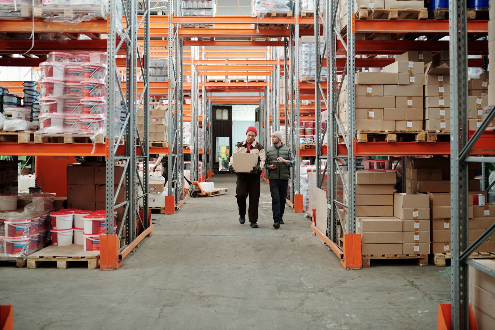 Two workers handle a package among stocked warehouse shelves