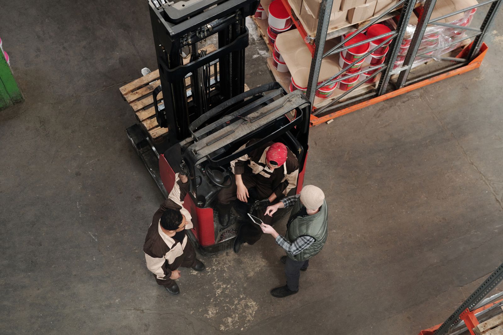 Workers discuss plans beside a forklift, seen from above