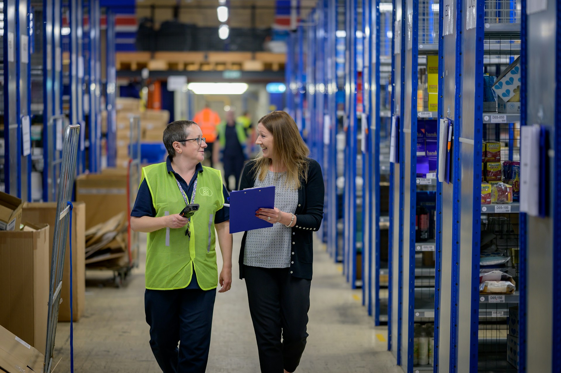 A C3 placed associate in a hi vis vest walks a distribution center aisle with a client supervisor holding a clipboard