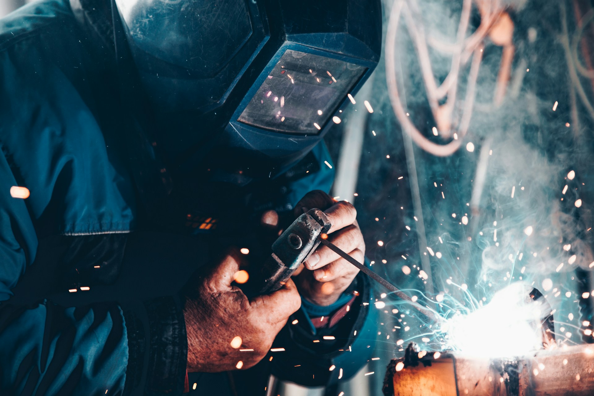 A welder in a dark visor works a bead as sparks fly